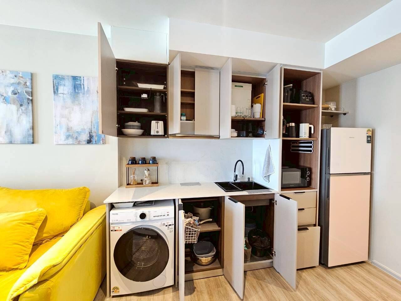 Cocina compacta con electrodomésticos integrados, lavadora y comedor con una silla amarilla.