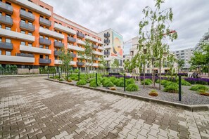Um edifício residencial com vários andares, varandas, um pátio pavimentado e jardins ajardinados.