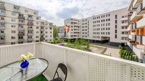 A balcony with a table and chair, a vase of flowers, and a view of modern apartment buildings. - Wrocław Gaj Studio - Balcony - by Rentujemy (Wrocław)