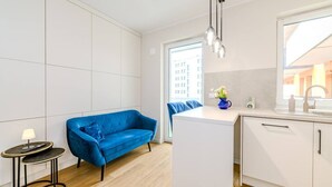 A modern kitchen with white cabinets, a blue sofa, and a small round table with a lamp. - Wrocław Gaj Studio - Balcony - by Rentujemy (Wrocław)