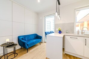 Cozinha moderna com armários brancos, um sofá azul e uma pequena mesa redonda com uma luminária.