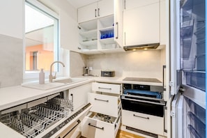 A compact kitchen with white cabinetry, a dishwasher, a built-in oven, and a window providing natural light. - Wrocław Gaj Studio - Balcony - by Rentujemy (Wrocław)