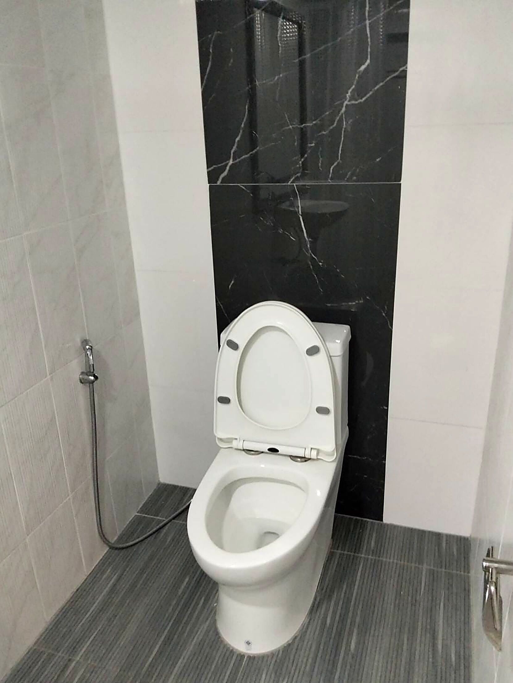 Un baño moderno con inodoro blanco, ducha y pared de mármol.