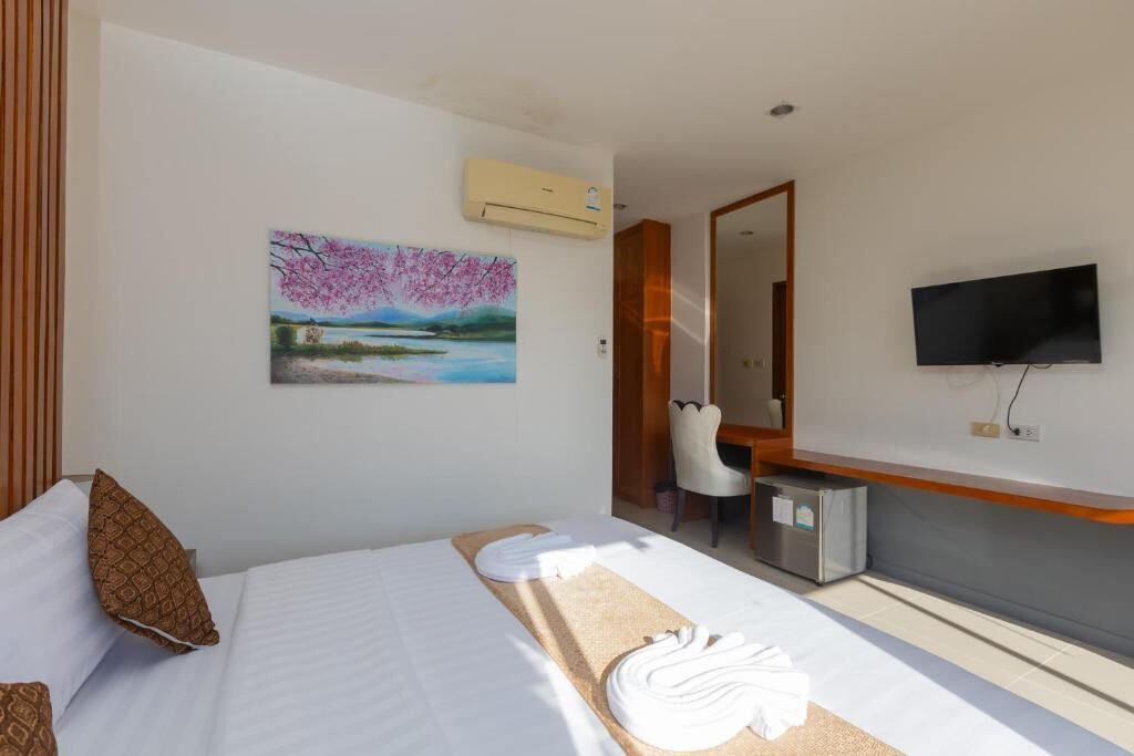 A hotel room with a bed, a painting, a TV, and a desk.