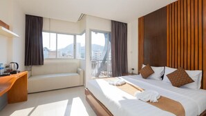 Ein Hotelzimmer mit Bett, einer Sitzecke, einem Schreibtisch und einem Balkon mit Blick auf die Stadt.