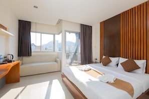 Ein Hotelzimmer mit Bett, einer Sitzecke, einem Schreibtisch und einem Balkon mit Blick auf die Stadt.