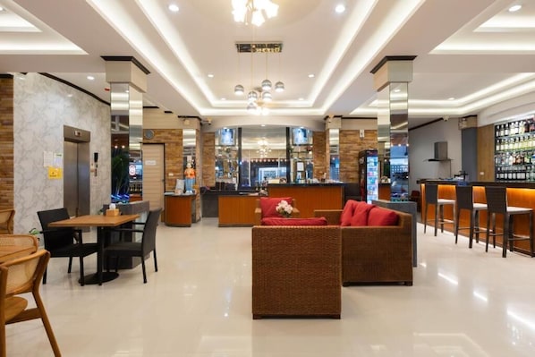 A modern hotel lobby with a reception desk, seating area, and bar.