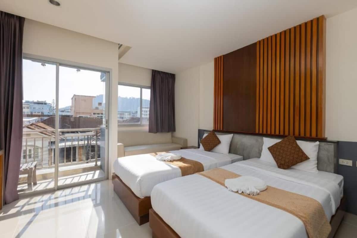 Habitación de hotel con dos camas, balcón y vista a la ciudad.