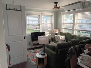 Ein Wohnzimmer mit einem grünen Sofa, einem Fernseher, einer Lampe und einem Fenster mit Jalousien.