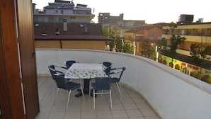 A balcony with a table and chairs, a tiled floor, and a view of buildings in the background. - Enjoy Your Holiday 200m From the Beach (Lignano Sabbiadoro)