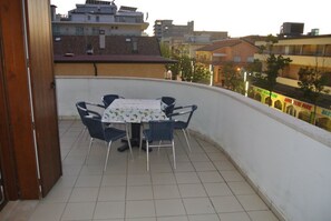 Ein Balkon mit Tisch und Stühlen, ein Fliesenboden und Blick auf Gebäude im Hintergrund.