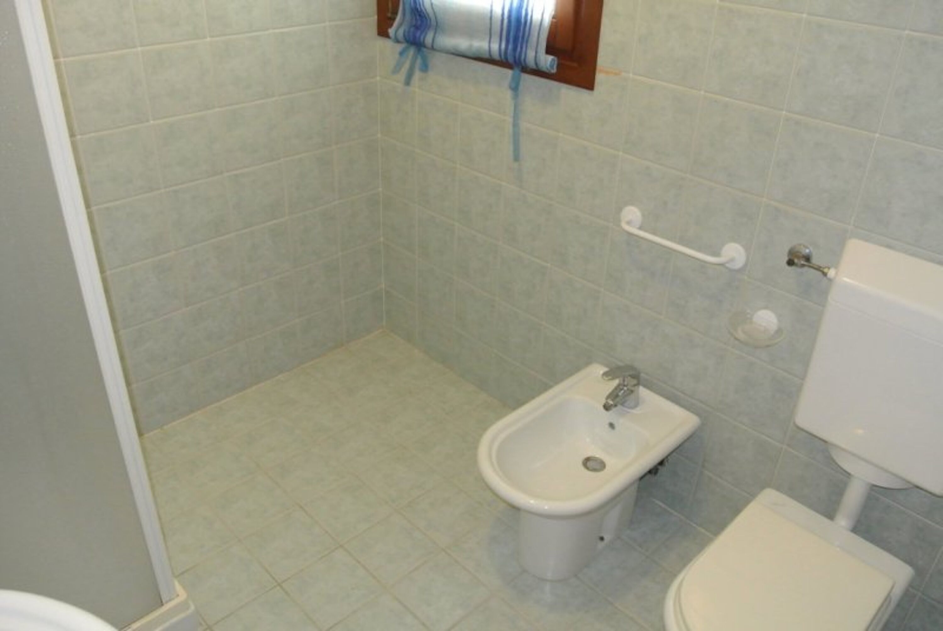 A small bathroom with a bidet, toilet, and a towel rack.