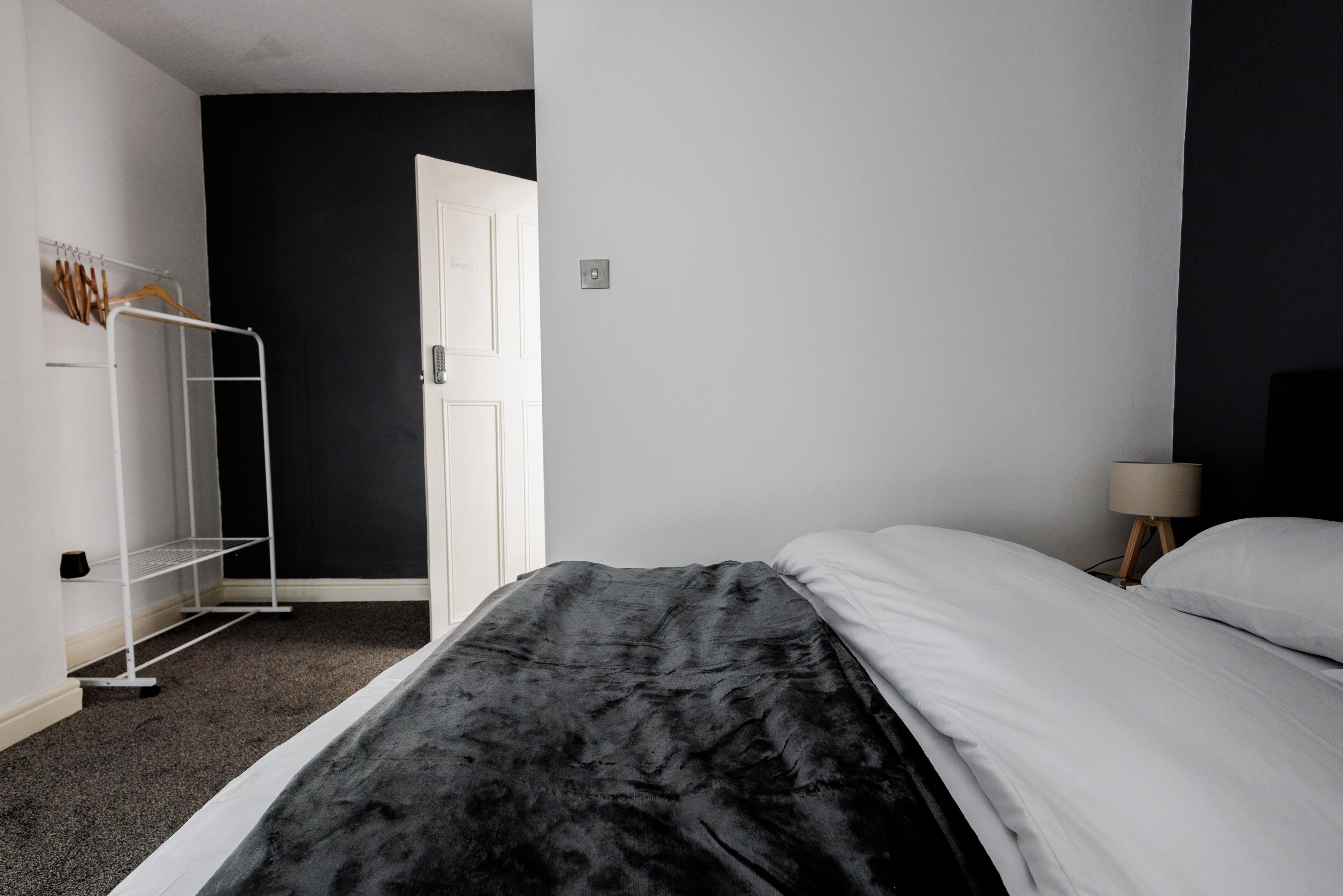 A bedroom with a bed, a white wardrobe, a black wall, and a door.