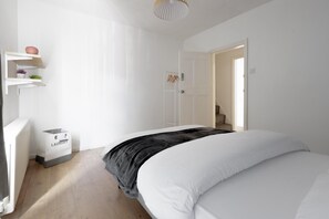 Ein Schlafzimmer mit einem Bett, einem Heizkörper, einem Wäschekorb und einer Tür zu einem anderen Raum.