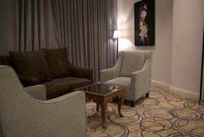 Ett hotellrum med en brun soffa, en grå fåtölj, ett litet träbord och en mönstrad matta.