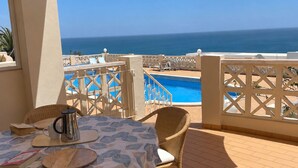 A terrace with a table set for two, overlooking a swimming pool and the sea. - 180 Degree Sea Views, Sunny Terrace & Quiet Pool (Luz)