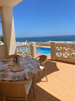 Eine Terrasse mit Tisch für zwei Personen, mit Blick auf einen Swimmingpool und das Meer.