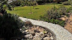 A landscaped garden with a paved pathway, various plants, and a view of the ocean. - 180 Degree Sea Views, Sunny Terrace & Quiet Pool (Luz)
