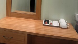 Un escritorio de madera con un espejo, una pequeña bandeja con una tetera y una taza.