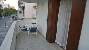 A balcony with a table and chairs, a door, and a view of the street. - Cozy Flat With Terrace 200m From the Beach (Lignano Sabbiadoro)