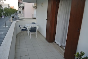 Ein Balkon mit Tisch, Stühlen, einer Tür und Blick auf die Straße.