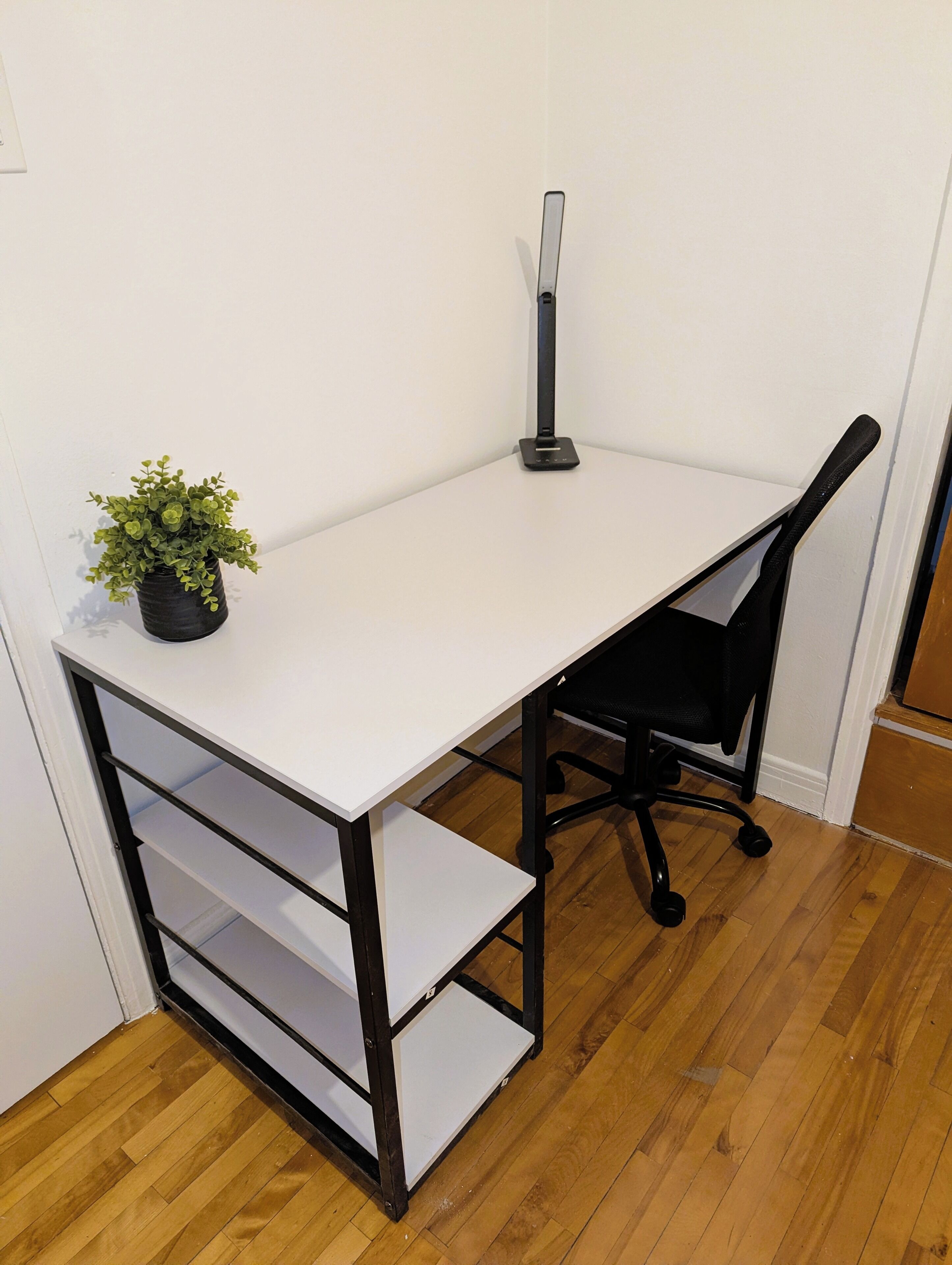 A white desk with black metal legs, a black office chair, and a small potted plant.