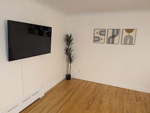 A room with a flat-screen TV mounted on the wall, a potted plant, and three abstract art pieces on the wall. - Private Room #1 - 5 min away - University - Fast WiFi (Trois-Rivières)