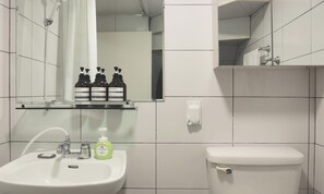 A bathroom with a sink, mirror, and toilet. There are three bottles of shampoo, a bottle of body wash, and a green bottle of soap on the sink. - Experience Seoul in a quiet area, just 4 minutes from Dapsimni Station. (Seoul)
