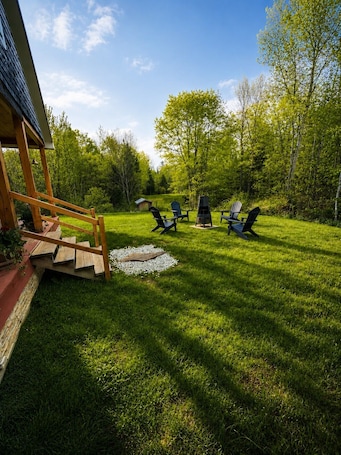 A wooden deck with a staircase leading to a covered area, surrounded by a well-maintained lawn and trees.. Once Upon a Time — A Peaceful Maine Escape