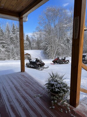 A wooden deck with a snow-covered landscape, two snowmobiles, and a thermometer.