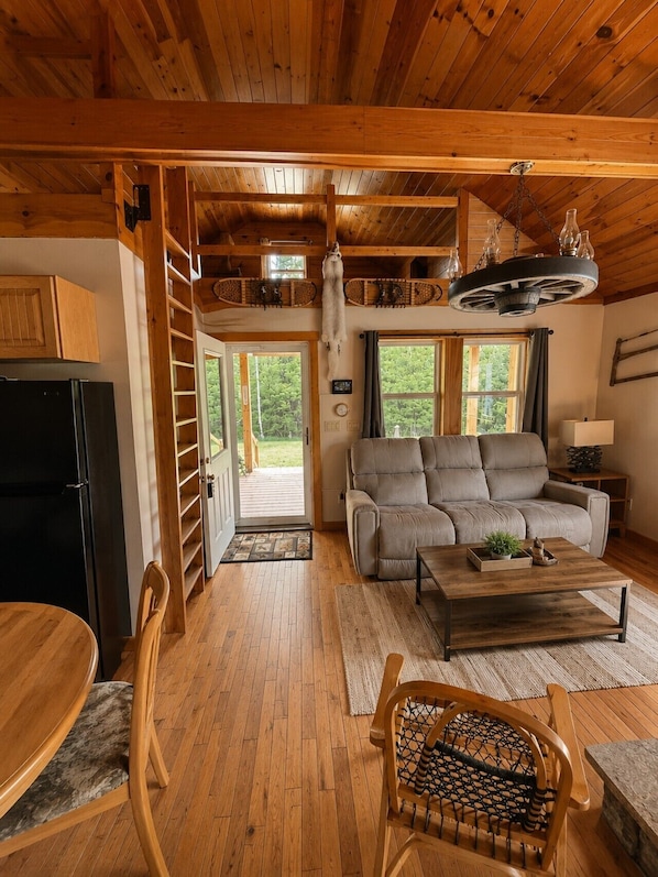 A wooden cabin interior with a sofa, dining table, and a chair with a woven seat.