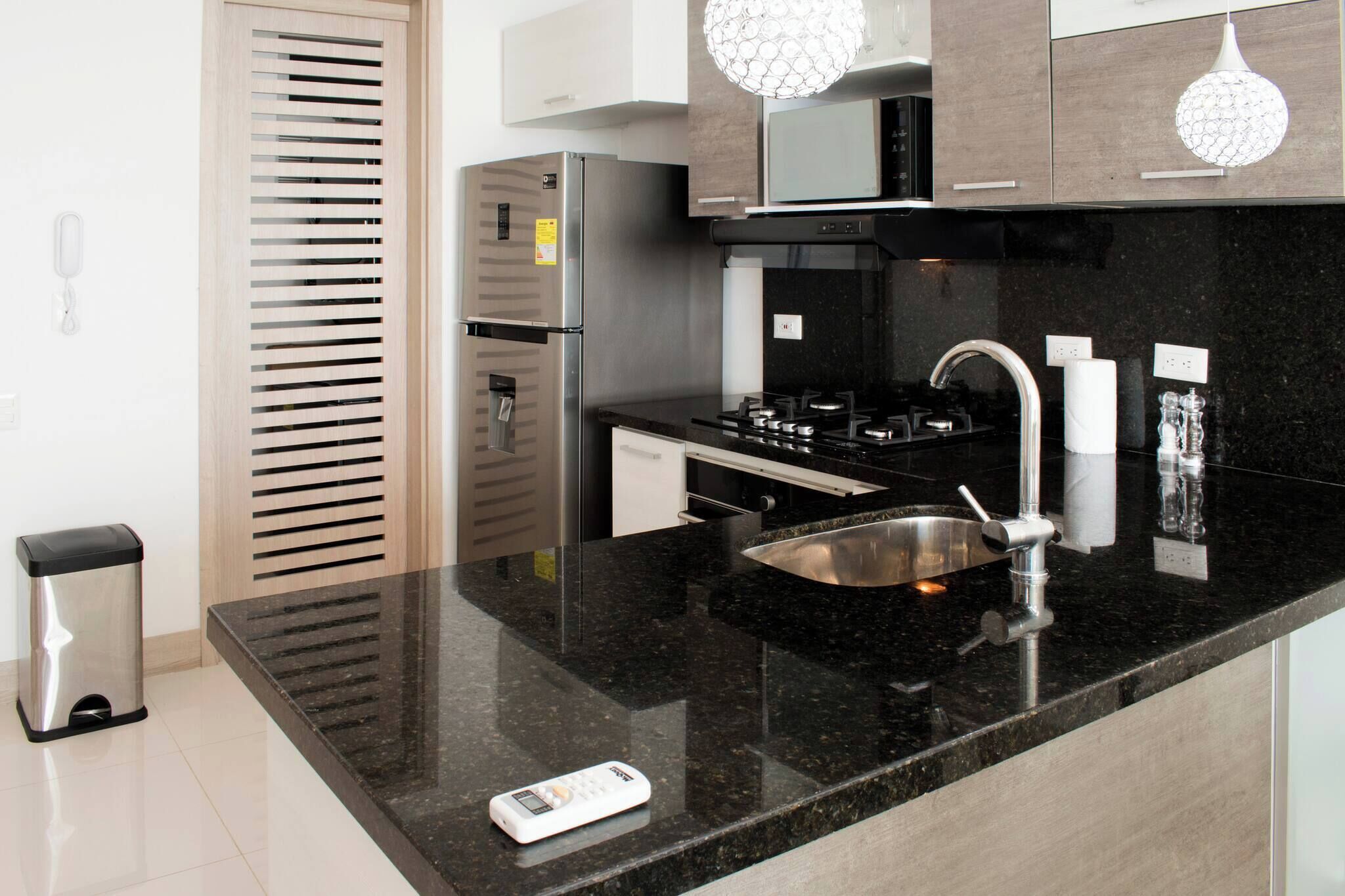 Una cocina moderna con un refrigerador de acero inoxidable, estufa a gas, un lavamanos y un microondas.
