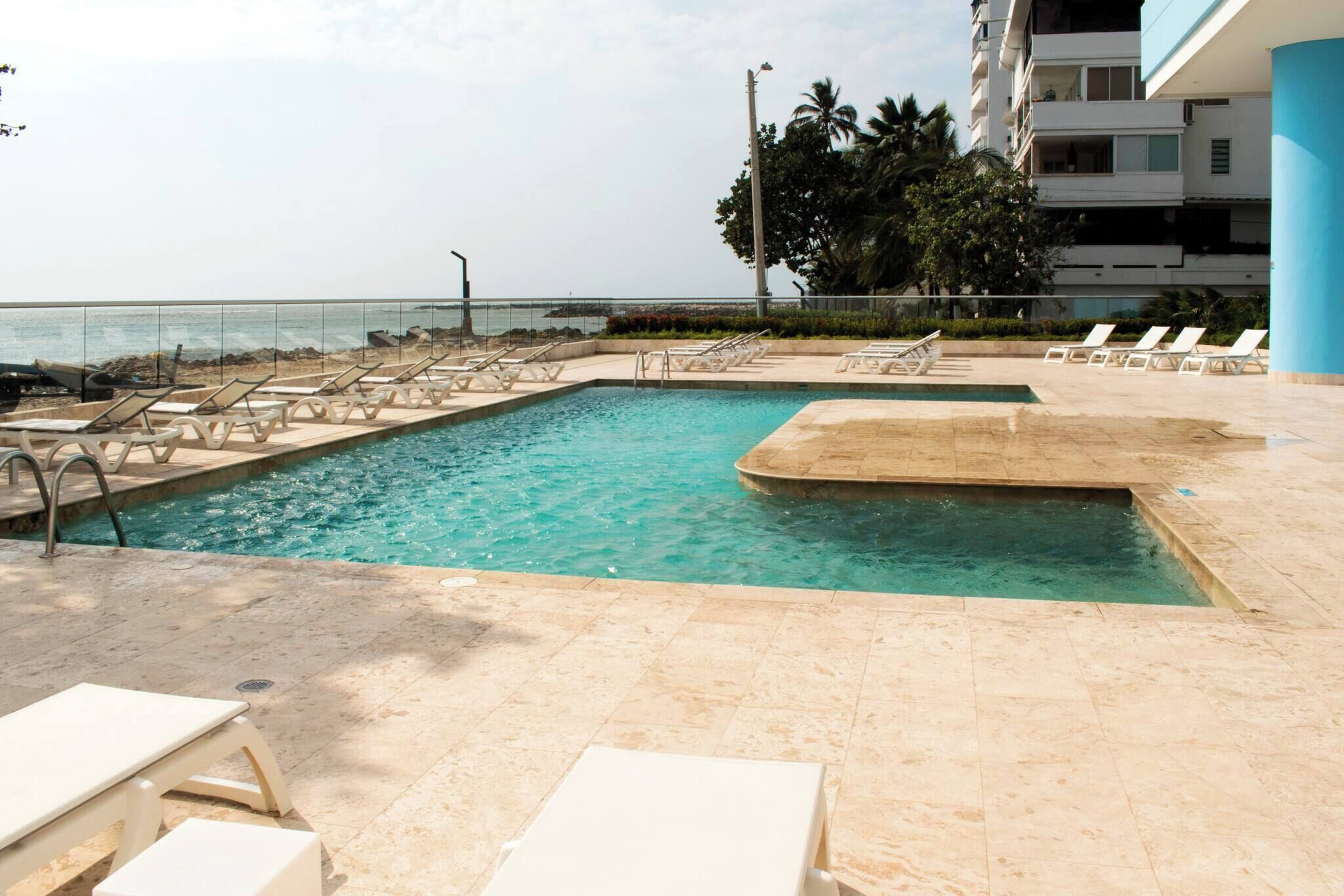Une piscine avec des chaises longues, une vue dégagée sur l’océan et un bâtiment doté de balcons.