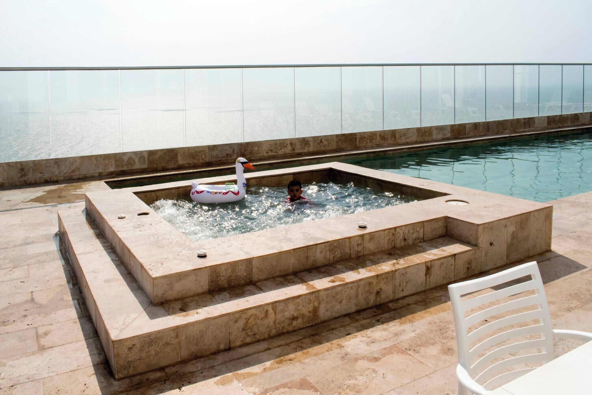 Une piscine avec un flotteur en forme de cygne, des marches menant à l’intérieur de la piscine et une vue sur la mer.