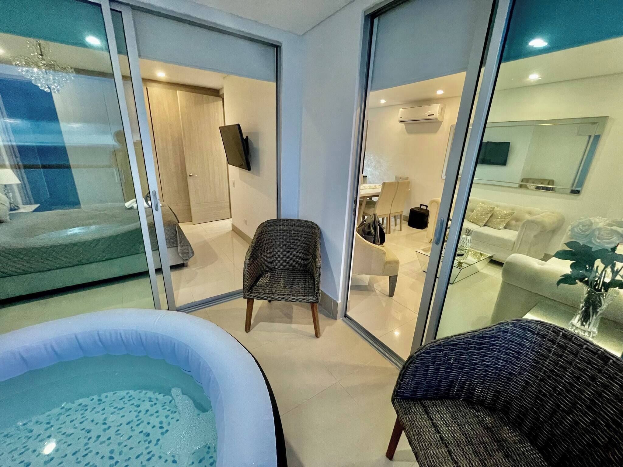 A modern living room with a glass partition, a wicker chair, a sofa, and a small table with a vase of flowers.