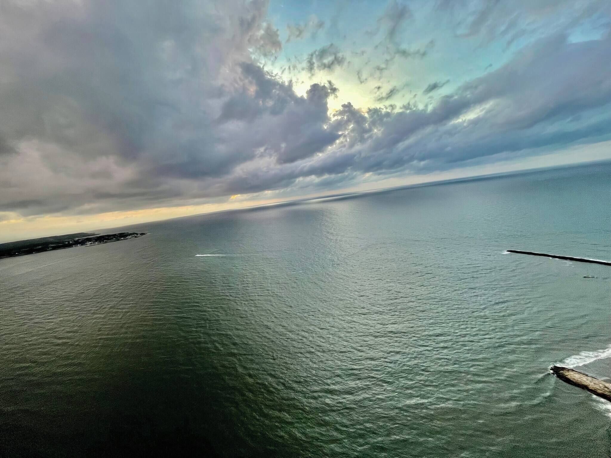 A coastal view with calm waters, a distant shoreline, and a partly cloudy sky.