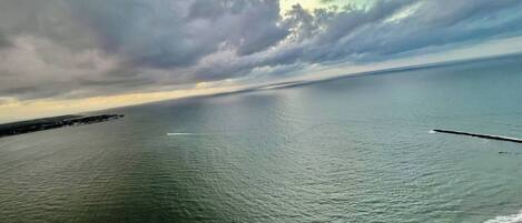 A coastal view with calm waters, a distant shoreline, and a partly cloudy sky.
