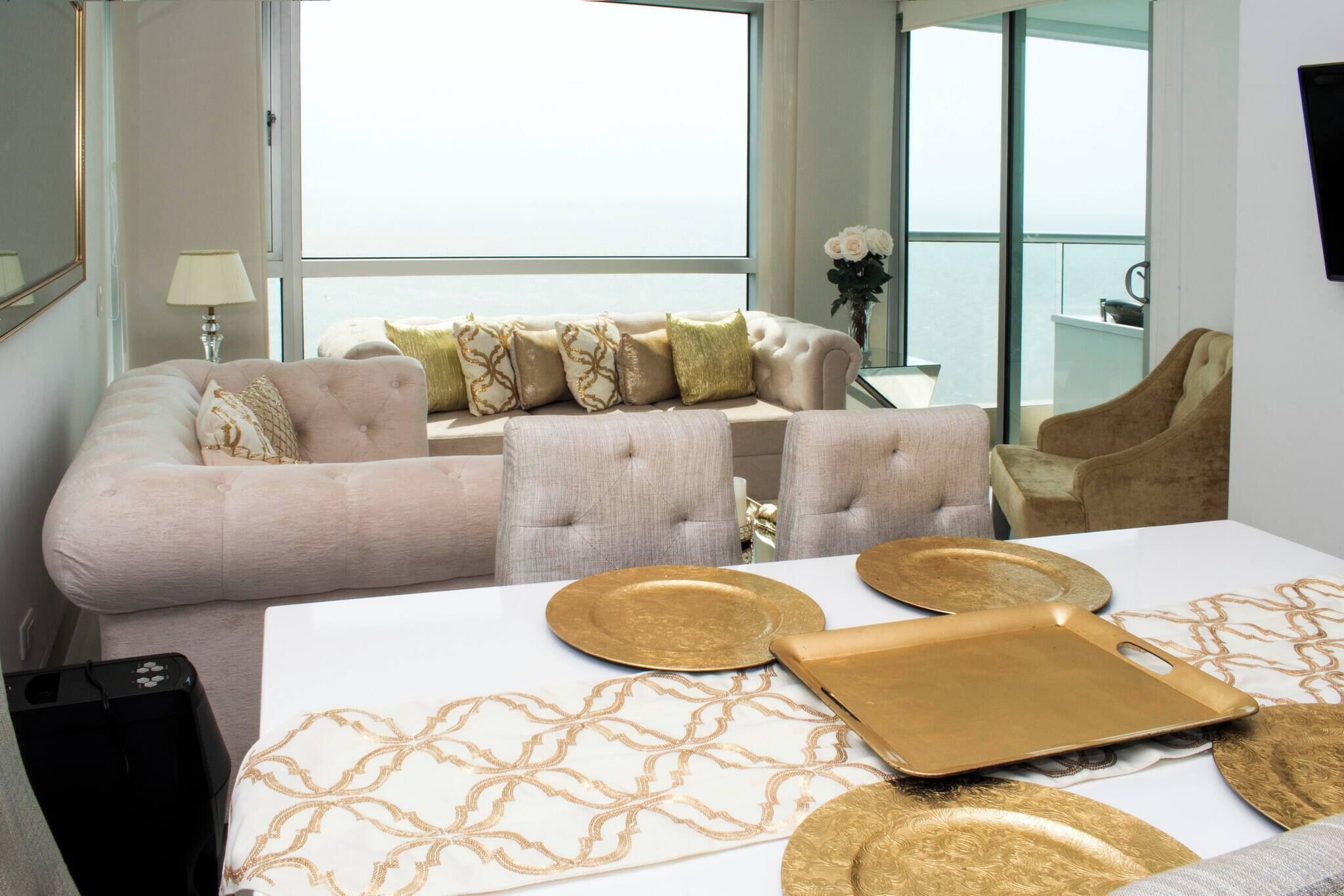 A modern living room with a sofa, armchairs, and a dining table with gold plates.