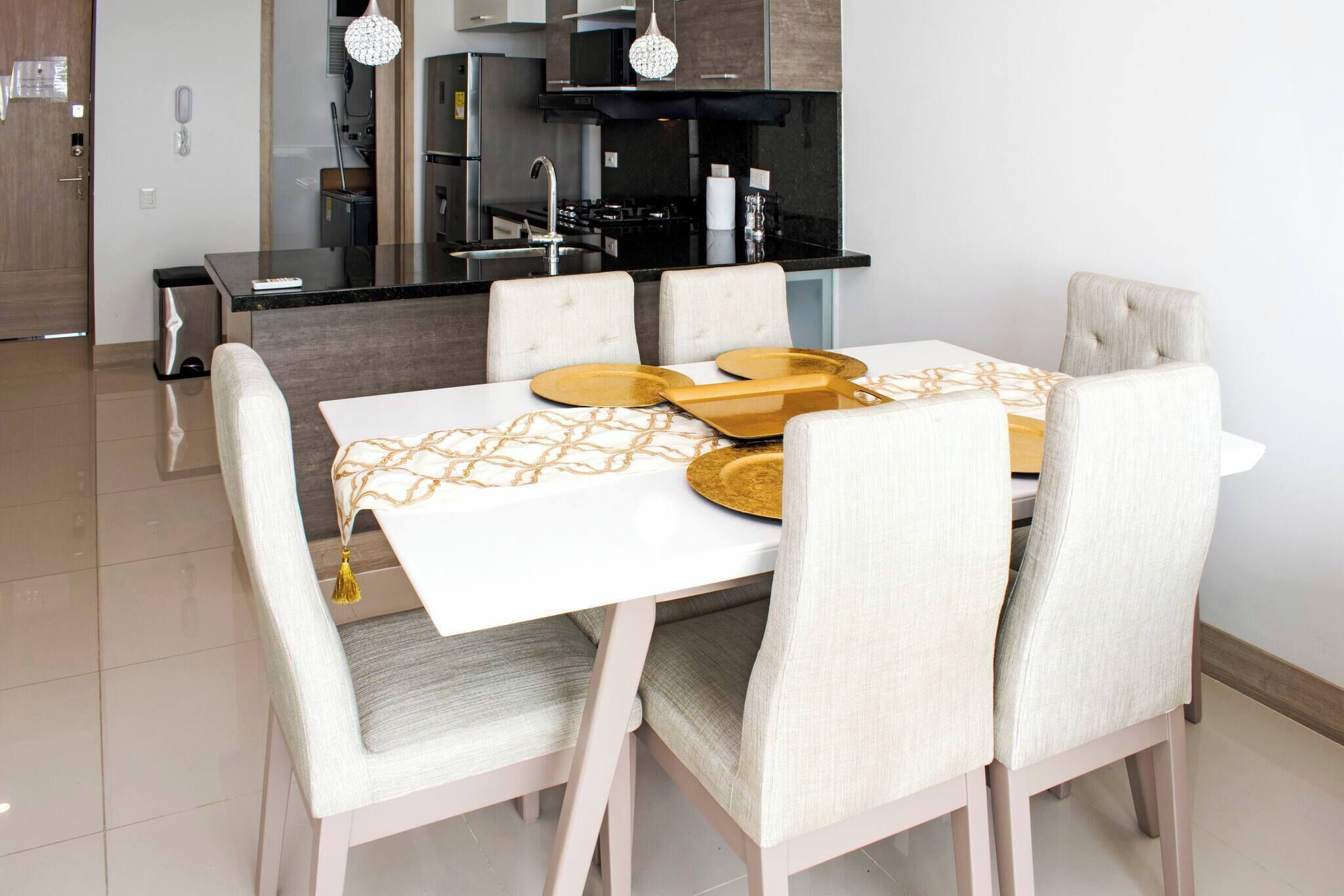 Un coin repas avec une table blanche, quatre chaises et une cuisine en arrière-plan.