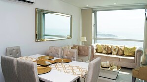 A modern living room with a dining area, a large window with a view, and a sofa with decorative pillows. - 1 Bedroom Sunset Luxury Apartment Private Jacuzzi (Cartagena)