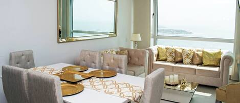A modern living room with a dining area, a large window with a view, and a sofa with decorative pillows.