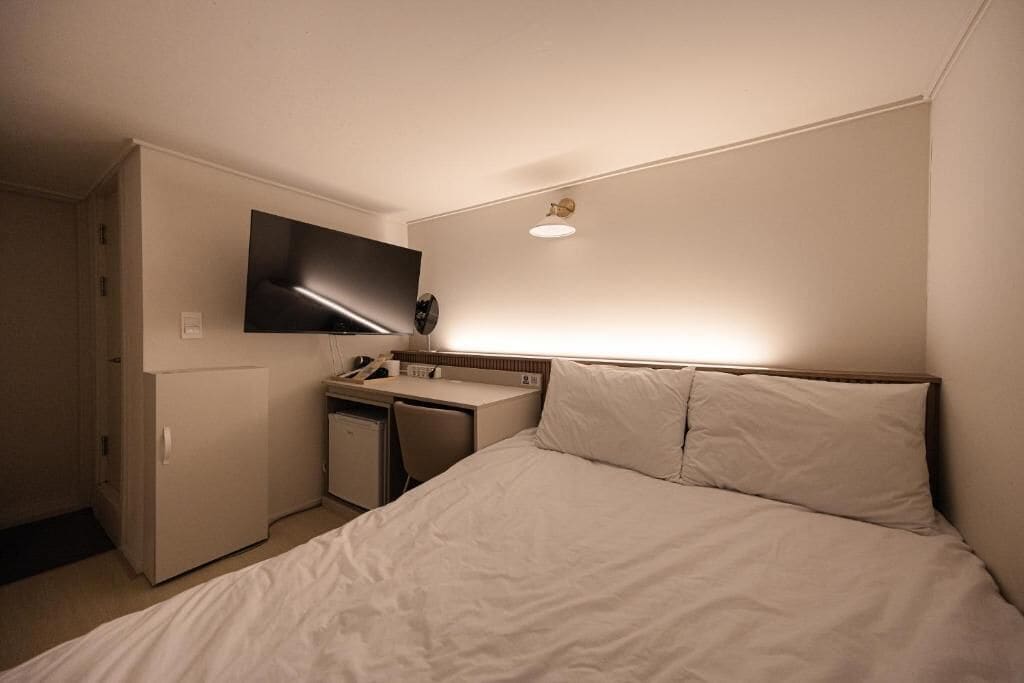A hotel room with a bed, a desk, a television, and a small refrigerator.