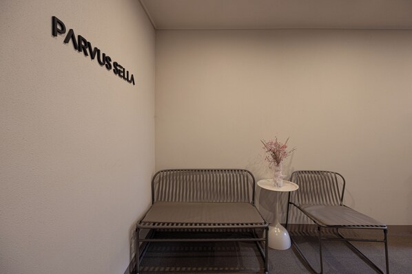 A room with a metal bench, a small table with a vase, and a wall sign reading 'PARVUSSELLA'.