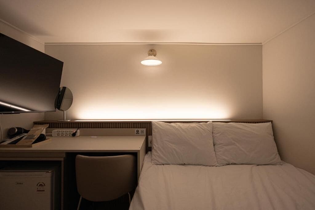 Habitación de hotel con cama, escritorio, silla y televisión de pantalla plana montada en la pared.