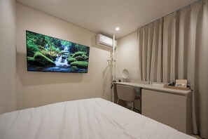Ett hotellrum med en säng, ett skrivbord med en stol, en tv som är monterad på väggen och ett fönster med gardiner.