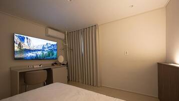 Quarto de hotel com cama, escrivaninha, cadeira, televisão e janela com cortinas.