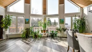 A sunlit room with large windows, wooden flooring, and multiple potted plants. - Campfire, Privacy, Stargazing minutes to Beaches/Orillia/Casino Rama (Orillia)