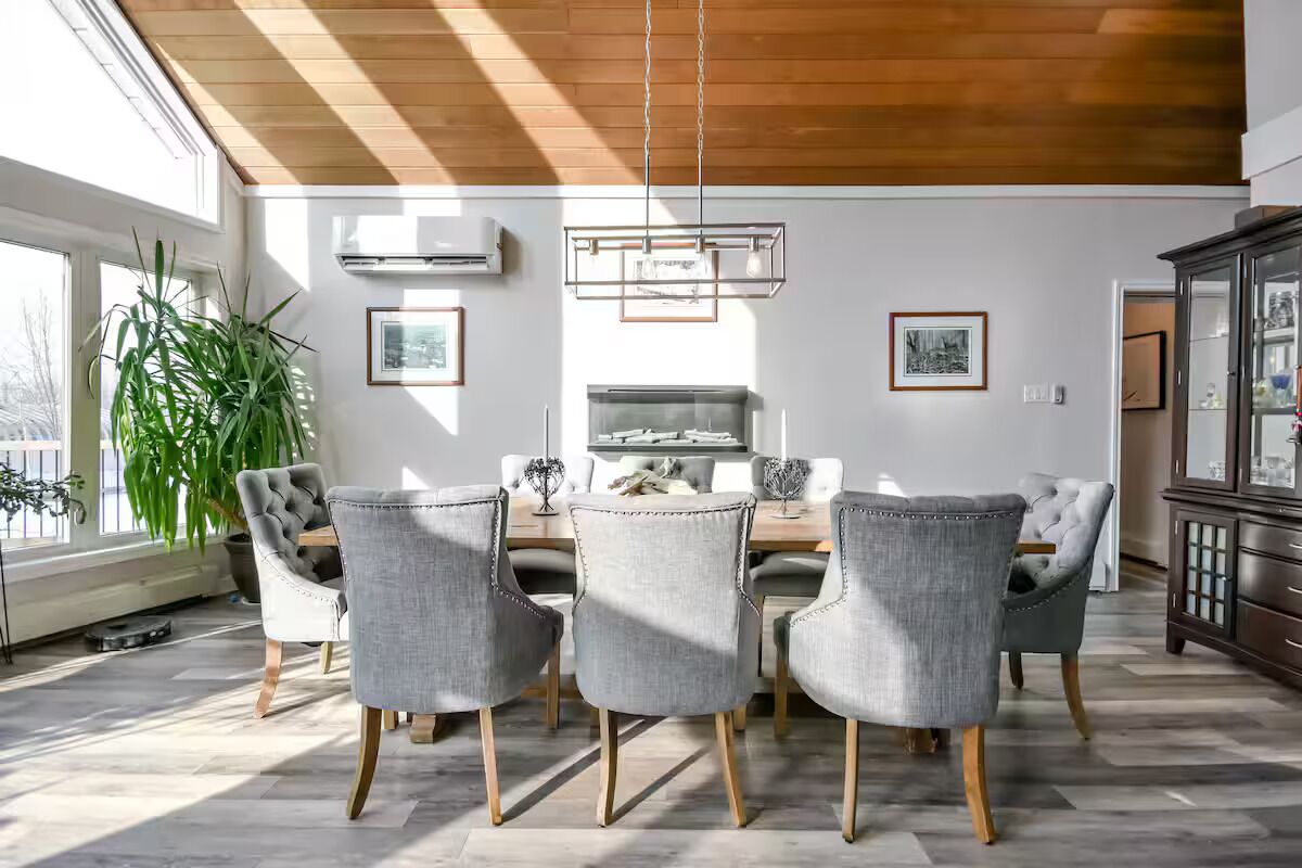 Zona pranzo con soffitto in legno, tavolo e sedie, e una pianta grande.