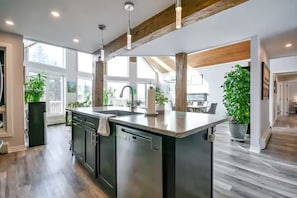 A modern kitchen with a large island, wooden beams, and large windows.
