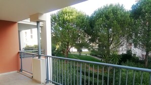 En balkon med gelænder, flisegulv og udsigt over en grøn have med træer og buske.